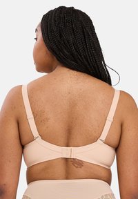 Reggiseno beige con spalline regolabili, tessuto morbido, chiusura posteriore a tre ganci e leggera imbottitura. Texture liscia con minimo dettaglio.