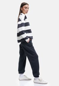 Oversized blurowy i biały sweter w paski, zestawiony z zwężającymi się ciemnymi dresami i białymi trampkami. Gładki materiał, luźny krój.