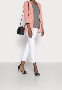 Lyserød blazer over en mønstret sort-hvid top, parret med hvide bukser og sorte strop høje hæle. Lille sort crossbody taske.