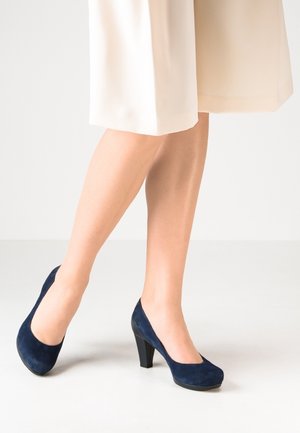 Tacones altos de ante azul marino con punta redondeada, tacón de bloque de altura media y textura suave, complementados por un diseño clásico.