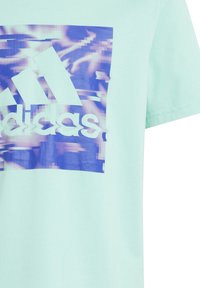 Světlý mátový bavlněný tričko s pixelovanou modro-fialovou grafikou a bílým logem adidas ve středu.