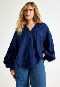 Marinblå, oversized blus med v-ringning, långa puffärmar och strukturerad tyg. Matchad med blå denimjeans.