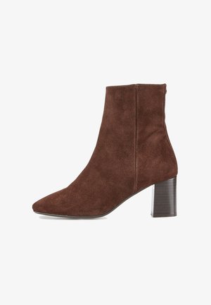 Bottine en daim marron avec un bout pointu, un talon bloc de hauteur moyenne et une fermeture éclair latérale. Texture lisse avec un léger éclat.