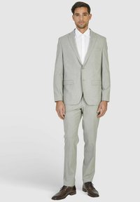 Lichtgrijze broekpak met een gestructureerde afwerking, bestaande uit een op maat gemaakt jasje en rechte broekspijpen, aangevuld met een wit overhemden en donkere schoenen.