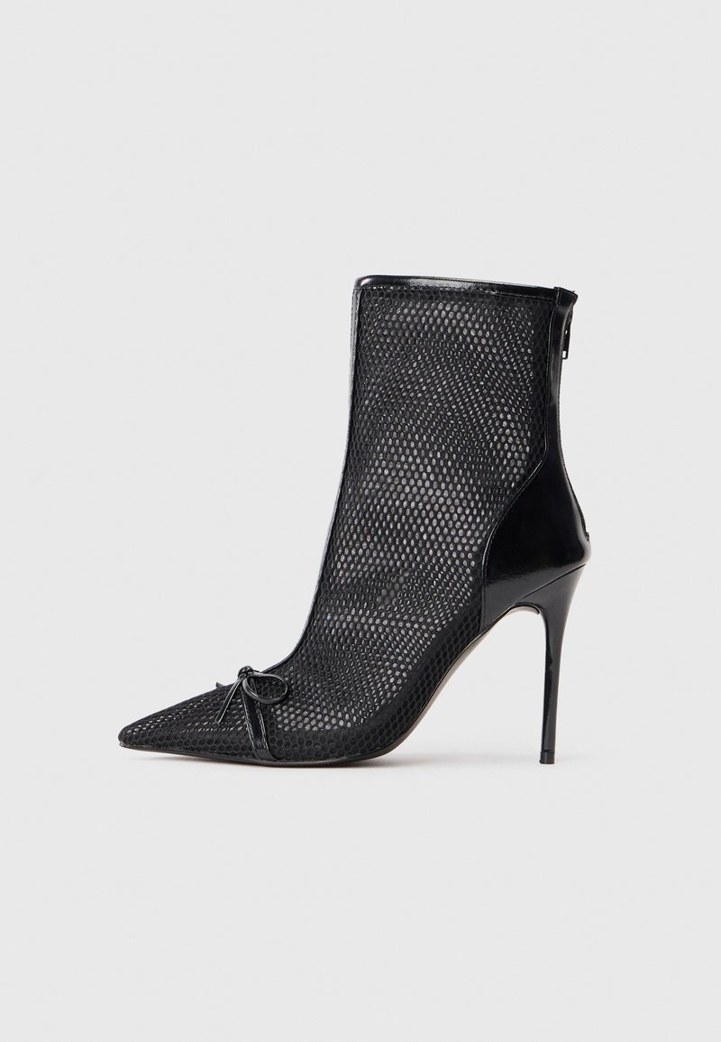 Svart mesh ankelstøvel med spiss tå, stiletthæl og dekorativ sløyfe foran. Har en blank finish på hælen og glidelåsen.