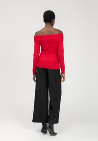 Rode off-shoulder trui met lange mouwen, gecombineerd met zwarte wijde broek en zwarte enkellaarsjes met hak. Eenvoudig ontwerp, gladde textuur.