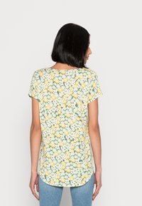 Camisa de manga curta floral em verde claro com margaridas amarelas e brancas. Com bainha arredondada e textura de tecido suave. Vista traseira exibida.