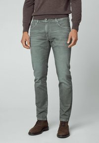 Jean en denim gris ajusté avec un design à cinq poches et un léger effet délavé. Associé à des bottes marron à lacets, complété par un pull foncé.