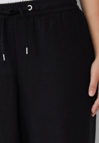 Schwarze Leinenhose mit elastischem Bund und Kordelzugverschluss. Glatte Textur und lockere Passform, geeignet für die Freizeit.