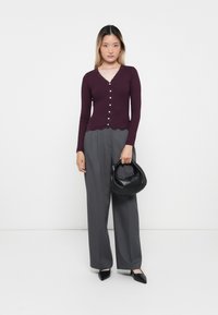 Cardigan bordeaux à manches longues avec des bords en dentelle et des boutons, accompagné d'un pantalon gris taille haute et d'un sac à main en cuir noir.