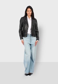 Černá kožená motorkářská bunda se zipy, spárovaná se světle modrými širokými džíny a černými lodičkami. Pod bundou je vidět bílá košile.