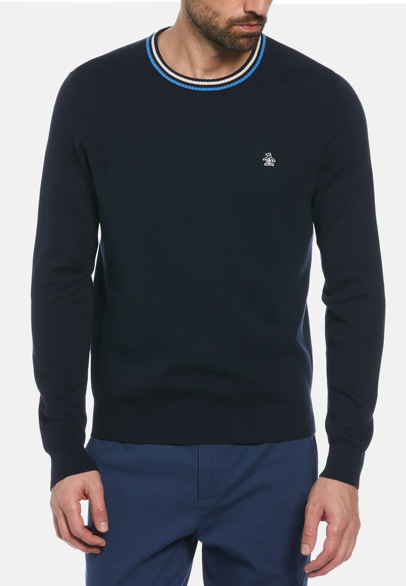 Pull en tricot marine avec un col rond, ornée de côtes rayées bleu et blanc. Logo de pingouin discret brodé sur la poitrine.