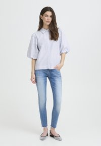 Gestreept overhemd met knopen en pofmouwen in blauw en wit; gecombineerd met aansluitende, lichtblauwe jeans en zwarte platte schoenen versierd met strass-steentjes.