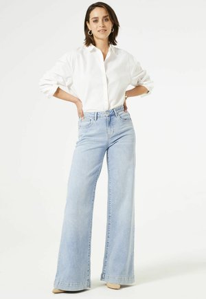 White button-up shirt with rolled sleeves, paired with light blue wide-leg jeans. The jeans feature a high waist and a faded finish.