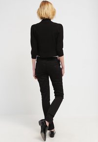 Černý krátký svetr s tříčtvrtečními rukávy, doplněný černými přiléhavými kalhotami a lesklými černými botami. Jednoduchý, elegantní design.