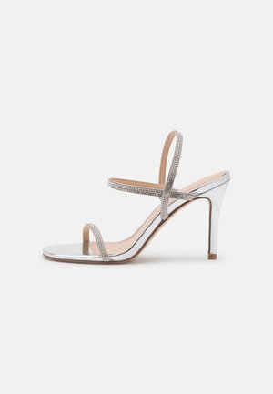 Srebrna metaliczna sandał wysoki na obcasie z dwiema cienkimi paskami i paskiem ozdobionym cyrkoniami. Posiada gładką teksturowaną podeszwę oraz obcas w kształcie szpilki.