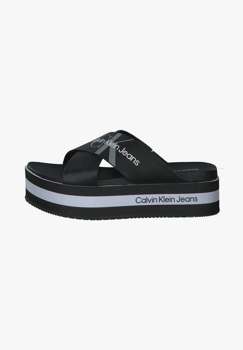 Sandale plateforme noire avec des brides croisées et un marquage blanc "Calvin Klein Jeans" sur les brides et le bord de la semelle.