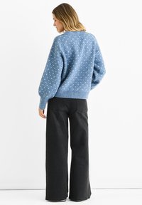 Light blue sweater with polka dots, ribbed cuffs, and hem, paired with wide-leg black pants. The fabric appears soft with a textured finish.