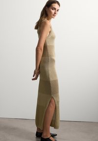 Strickkleid in Gold mit tailliertem Schnitt und seitlichem Schlitz. Verfügt über eine Mischung aus strukturierten Abschnitten und glatten Paneelen. Einfaches Trägerdesign.