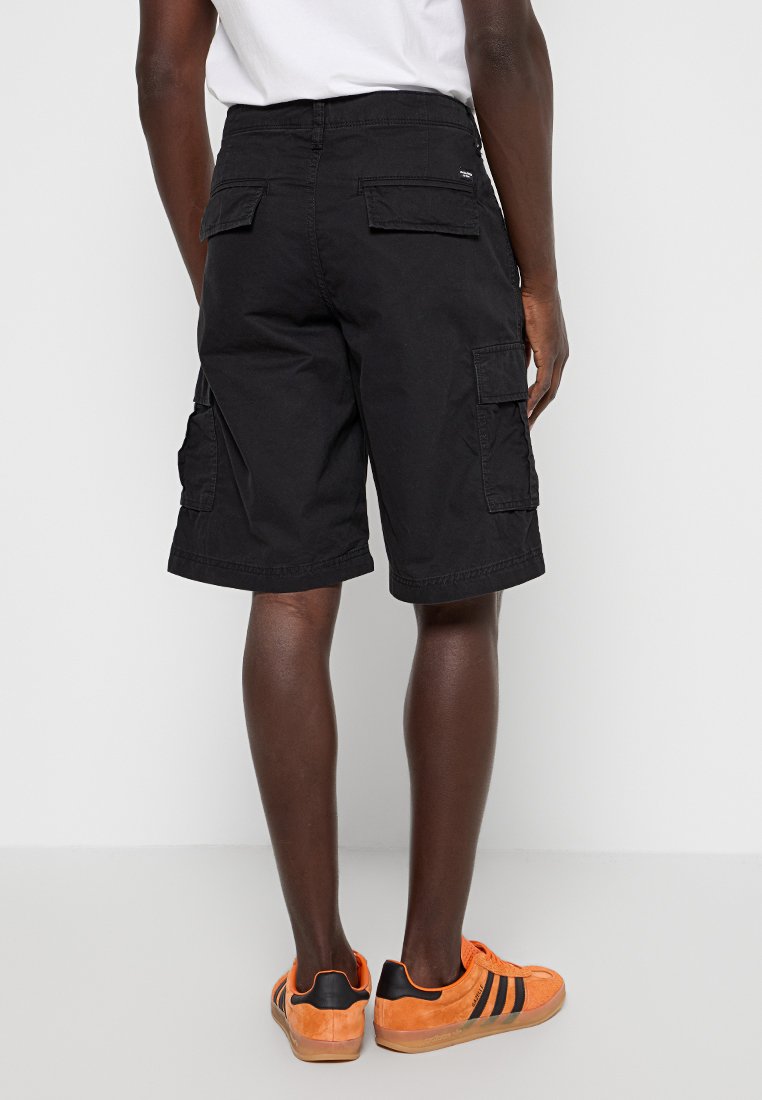 Schwarze Cargo-Shorts mit Rücken- und Seitentaschen, aus strapazierfähigem Stoff gefertigt. Getragen mit orangen Sneakers mit schwarzen Akzenten.