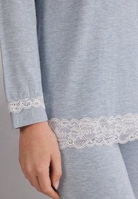 Jasnoniebieski, długi rękaw, ubranie o miękkiej teksturze, z białą koronkową lamówką wokół mankietów i dolnego brzegu.
