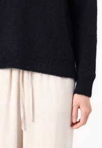 Pull en laine bleu marine à la coupe ample et finition texturée, associé à un pantalon en lin beige clair avec taille élastique.