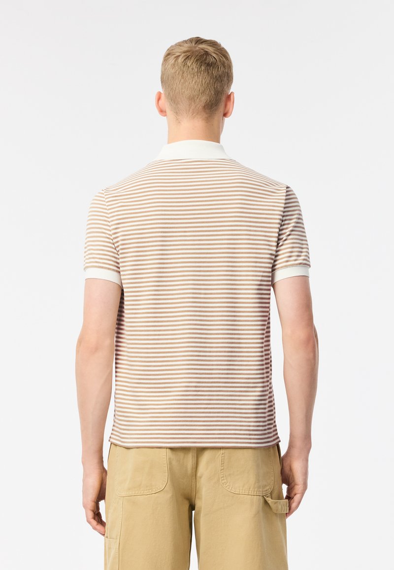 Polo rayé aux couleurs crème et beige, à manches courtes et col blanc. Présente un design légèrement ajusté. Semble être en tissu doux.