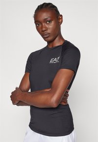 Zwart sportshirt met korte mouwen, met een gestructureerde stof en het EA-logo op de borst. Glad, getailleerd ontwerp voor actieve kleding.