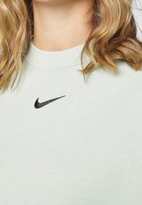 Světle mátově zelená mikina vyrobená z měkké látky s kulatým výstřihem a černým vyšívaným logem Nike na hrudi.