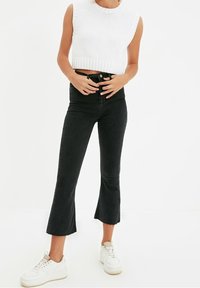 Vitt stickat kort linne i kombination med svarta, högmidjade jeans med utsvängda ben och rå fåll, kompletterat med vita sneakers.