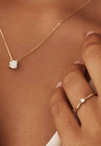 Gouden ketting met een bloemenhanger en gouden ring met een enkele diamant. De hanger en diamant zijn helder met een gepolijste afwerking.