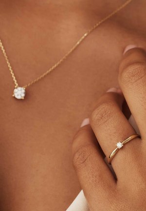 Collier en or avec un pendentif floral et une bague en or avec un seul diamant. Le pendentif et le diamant sont clairs avec une finition polie.