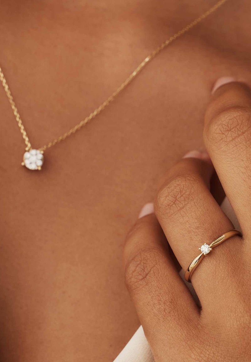 Gouden ketting met een bloemenhanger en gouden ring met een enkele diamant. De hanger en diamant zijn helder met een gepolijste afwerking.