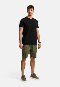 T-shirt en coton noir, shorts cargo verts olive et baskets grises. Les shorts cargo ont des poches et un patch logo. Tenue simple et décontractée.