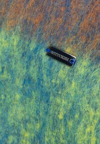 Wielobarwny filc w odcieniach niebieskiego, zielonego i pomarańczowego, z metalową metką "WITTCHEN" przymocowaną niebieską nicią.