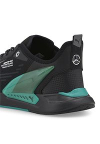 Svart och teal Puma-sneaker med AMG Petronas Formula One Team-typografi och Mercedes-logotyp på hälen, som visar sid- och bakdetaljer.