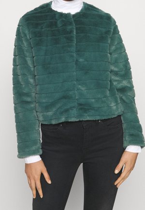Chaqueta corta de piel sintética en color verde azulado con rayas horizontales, cuello redondo, sin cierres y mangas largas, combinada con pantalones negros.