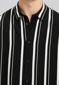 Svartvit randig skjorta med knappar, med krage och svarta knappar, tillverkad av ett mjukt tyg med en matt yta.