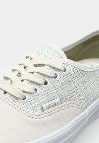 Witte canvas sneakers met een gestructureerde bovenkant, crèmekleurige veters en VANS-logo. Glad rubberen zool en oogjes voor ventilatie. Klassiek laag model.