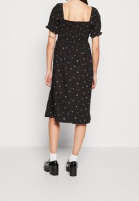 Robe noire avec des manches courtes bouffantes et un corsage froncé, ornée d'un motif floral. Portée avec des chaussettes blanches et des chaussures à plateforme noires.