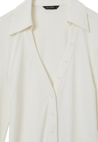 Camicia bianca con colletto a punta, caratterizzata da una texture liscia e sette bottoni sulla parte anteriore. Etichetta con la scritta "CALLIOPE" taglia S.
