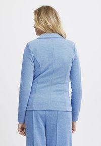 Giacca tailored azzurra chiara con maniche lunghe e colletto a caduta, realizzata in un tessuto testurizzato, con una silhouette aderente e dettagli delle cuciture posteriori.