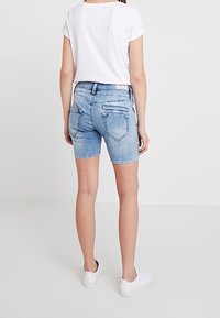 Jasnoniebieskie szorty dżinsowe o średnim stanie. Posiadają tylne kieszenie i teksturowany pas. W połączeniu z klasyczną białą koszulką.