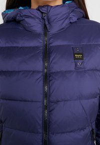 Giacca a piumino blu navy con cappuccio, dotata di zip frontale, motivo trapuntato orizzontale e toppa con logo vicino alla zip. Tessuto con texture.