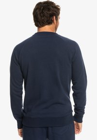 Navy blue sweatshirt with a ribbed crew neck, long raglan sleeves, and a textured finish. Features a wide elastic hem and cuffs.