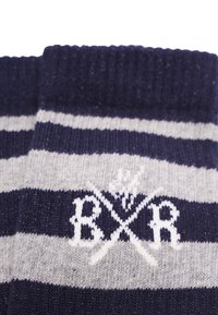 Stribede sokker i marinblå og grå med en blød tekstur; har hvide broderede bogstaver og krydsede elementer i designet.