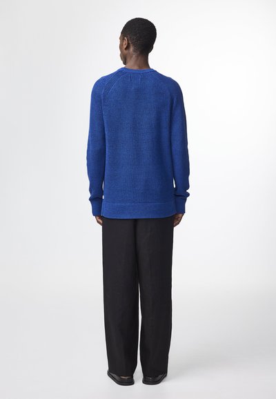 Strickpullover in Blau mit rundem Halsausschnitt und gerippten Bündchen, kombiniert mit locker sitzenden schwarzen Hosen. Einfaches, lässiges Design.