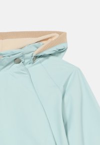 Αντιανεμικό μπουφάν ανοιχτού μπλε χρώματος με μπεζ κουκούλα επενδυμένη με fleece, με δύο πλευρικά κουμπιά με τρουκς και εμφανείς ραφές.