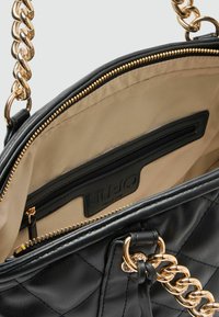 Zwarte gewatteerde leren handtas met gouden kettingriem. Het interieur heeft een beige voering, één ritsvak en een merklabel van LIU JO Milano.