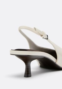 Escarpin à bride arrière beige clair avec talon haut étroit et incurvé effet bois et bride à boucle réglable.